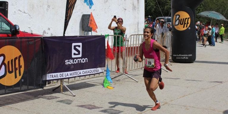 Corredora cruzando la meta en la carrera Trail de la Mixteca Oaxaqueña, con un letrero de Buff y Salomon en el fondo.